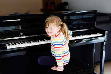 Beautiful little toddler girl playing piano in living room. Cute preschool child having fun with...