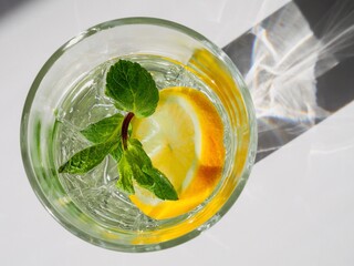 Top view of the glass of water, lemon and mint. Wellness, healthy food, drink, diet, detox. Fresh summer lemonade. Shadows on white background. Sun lighting. Copy space