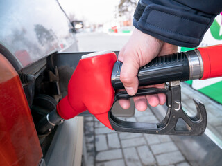 A man refuels the car with gasoline. Gas station, a man holding a red refueling gun inserted into the gas tank, close-up.