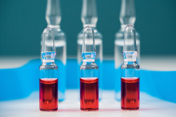 Close-up of glass ampoules in a row with a red antibiotic or vitamin preparation for the treatment and prevention of diseases. Horizontal.