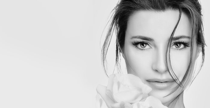 Beauty and skincare concept. Attractive woman with clean fresh skin and white roses near to cheek. Monochrome close-up beauty model face