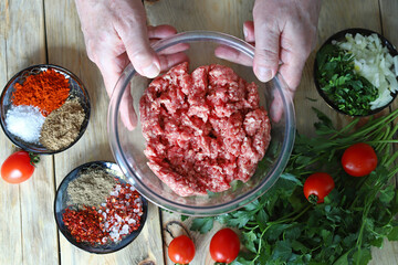 Minced meat in a bowl and the hands of the cook. Cooking minced meat for burgers or grilling.