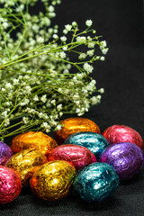 chocolate easter eggs and dried flowers on black background