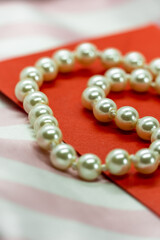 pearl necklace and red envelope on a pale pink background with white stripes