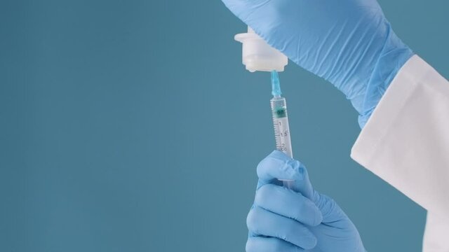 A paramedic on a blue background draws from a transparent bottle into a syringe the required dose of medicine for viruses and infections.