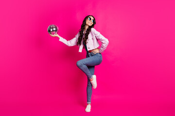 Full size profile photo of optimistic brunette lady hold disco ball dance wear spectacles top jeans jacket sneakers isolated on pink background