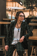 Beautiful brunette woman in a classical costume and white T-shirt. Sits on a chair in restaurant. Looks away. Glasses.