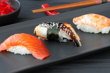 Nigiri sushi with salmon, eel and prawn served on black ceramic plate