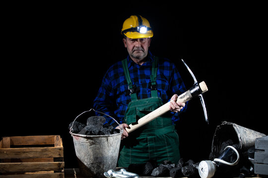 A miner with a pickaxe in his hand stands by a bucket full of black coal on a black background