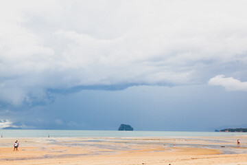 Fototapeta na wymiar Empty moody Asian Thailand beach with small number of leisure travellers and tourists. Summer holiday concept in New Normal period. Scenic summer nature photo with a thundercloud. Copy space