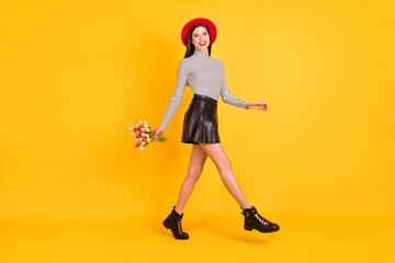 Fototapeta na wymiar Full length photo of charming cute woman walk empty space hold flowers isolated on bright yellow color background