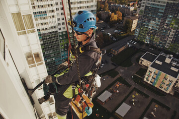 Industrial mountaineering worker hangs over residential facade building while washing exterior facade glazing. Rope access laborer hangs on wall of house. Concept of urban works. Copy space for site