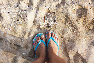 Top view woman feet on golden sandy beach. Selfie of legs in sandals shoes on seashore background....