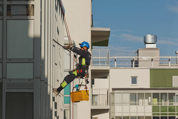 Industrial mountaineering worker hangs over residential facade building while washing exterior facade glazing. Rope access laborer hangs on wall of house. Concept of urban works. Copy space for site