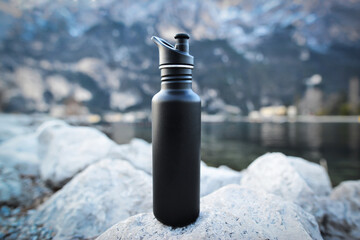 Close-up black of steel eco thermo water bottle on the background of the lake in the mountains....