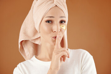 Portrait of pretty young woman with undereye patches making silence gesture and looking at camera