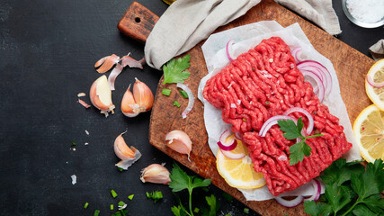 Fototapeta na wymiar Raw minced meat with spices, vegetables and herbs on dark background.