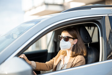Naklejka premium Young woman driving car with protective mask and sunglasses on her face. Healthcare, virus protection, allergy protection concept. 