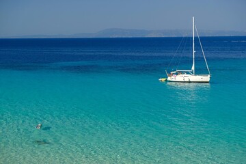 Chalkidiki, Greece - August 14, 2017 : A sailboat and a single person swimming in the crystal clear...