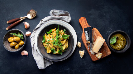 Pasta spaghetti with homemade pesto and fresh basil leaves on dark background. Italian cuisine concept.