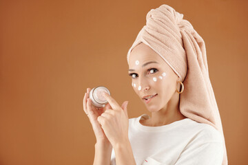 Beautiful young woman applying rejuvenating cream enriched with vitamins after taking night bath,...