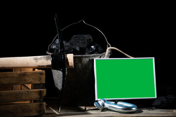 Black charcoal lies on a wooden platform and a bucket with a green sign posted to be filled