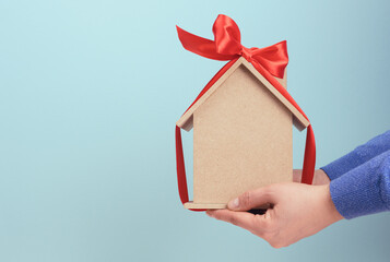 female hands hold a model of a wooden house tied with a red silk ribbon on a blue background
