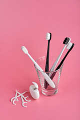 Fashionable toothbrush with soft bristles. Popular toothbrushes. Hygiene trends. Oral hygiene kit. Toothbrushes in glass, floss thread and toothpicks on a pink background
