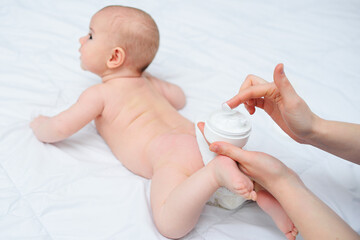 mother's hand applies a moisturizing baby cream to the baby boy's skin. Hygiene of the newborn child.