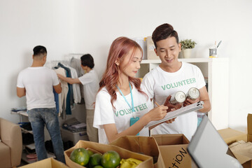 Volunteers working in charitable foundation taking notes in document and describing all food and...