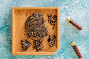 pressed green tea on wooden stand and puer knife on abstract aqua blue background.