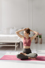 Girl take exercise. A young woman sits on a mat and weaves her hair before sports workout.