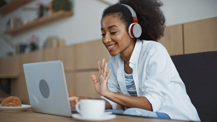 happy african american businesswoman in wireless headphones having video call in cafe