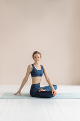 Fototapeta premium Girl does yoga. Young woman practices asanas on a beige one-ton background.