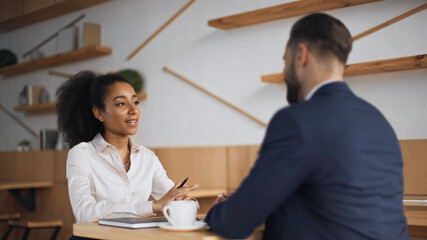 african american businesswoman talking with blurred businessman in suit during meeting on cafe