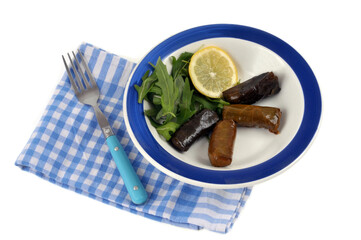 Feuilles de vigne farcies servies dans une assiette avec une rondelle de citron et de la salade roquette en gros plan sur fond blanc