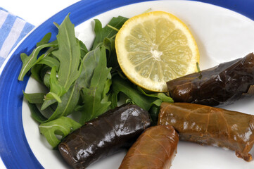 Feuilles de vigne farcies servies dans une assiette avec une rondelle de citron et de la salade roquette en gros plan