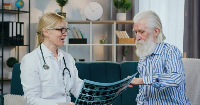Good-looking happy smiling experienced female doctor is contented from male patient's x-ray scan and giving him high five during home visit