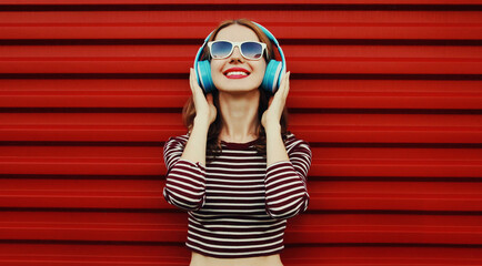 Portrait of happy young woman with wireless headphones listening to music on a red background