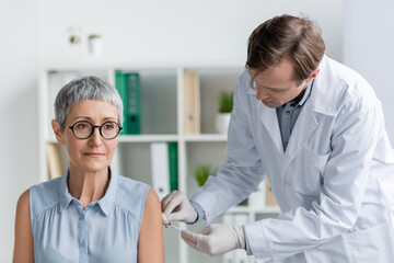 Obraz premium Middle aged patient sitting near doctor in latex gloves doing vaccination