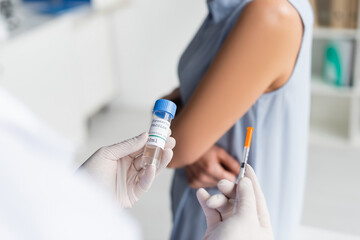 Cropped view of doctor holding coronavirus vaccine and syringe near woman on blurred background