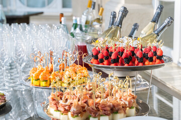 Wedding day recepton. Buffet table. Catering service. Plates with sweet canape with berries, raspberry, blackberry, ham,shrimp.Delicious gourmet food for guests.Many glasses,bottles of champagne,wine