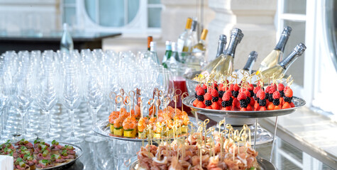 Wedding day recepton. Buffet table. Catering service. Plates with sweet canape with berries, raspberry, blackberry, ham,shrimp.Delicious gourmet food for guests.Many glasses,bottles of champagne,wine