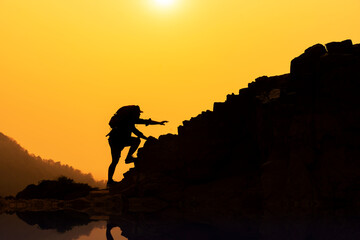 Silhouette of a young man who has successfully climbed a mountain, the concept of a mountain climbing inspiration, the movement of a beautiful sunset in the Asian Mekong River