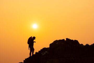 Naklejka premium Silhouette of a young man who has successfully climbed a mountain, the concept of a mountain climbing inspiration, the movement of a beautiful sunset in the Asian Mekong River