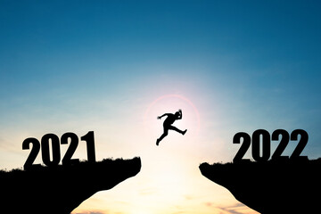Silhouette man jumping from 2021 cliff to 2022 cliff with blue sky and sunlight, preparation new challenge business target and life for new year.