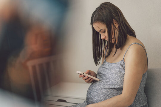 Happy charming pregnant woman using mobile phone. Pregnant Woman. Waiting for Baby. Pregnant Young Girl. Relaxing at Home.