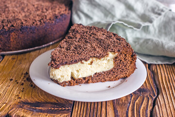 A piece of homemade chocolate pie with curd filling on a plate on a wooden table, close-up