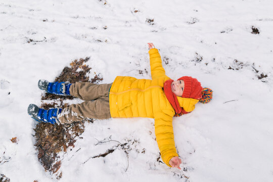 Cheerful boy lying on the snow, making a snow angel.