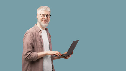 Happy albino man using laptop and looking with smile to camera over turquoise background, panorama...